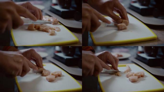高加索年轻男性的特写手正在厨房里的塑料白板上切新鲜的鸡肉。爱好烹饪，单身汉做晚餐。一个孤独的人准备家