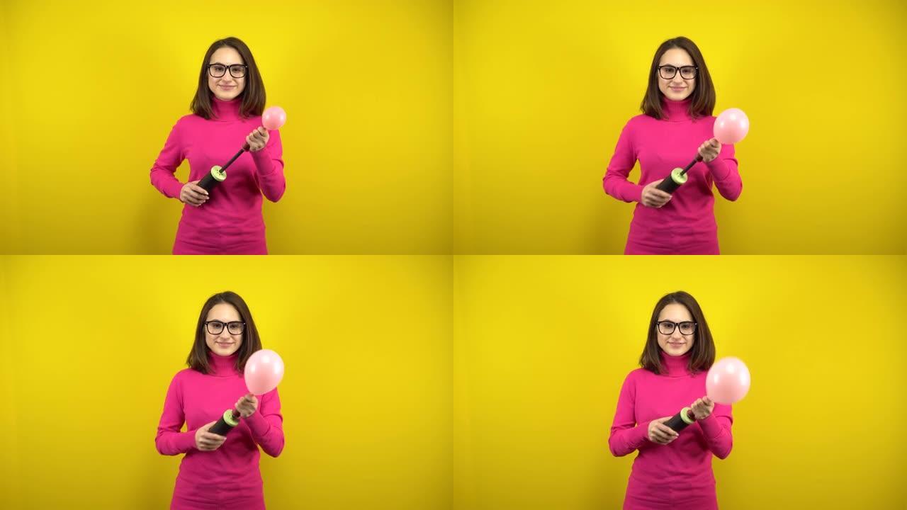一名年轻女子用泵给一个粉红色的气球充气，它在黄色背景上爆裂。穿着粉色高领毛衣和眼镜的女孩。