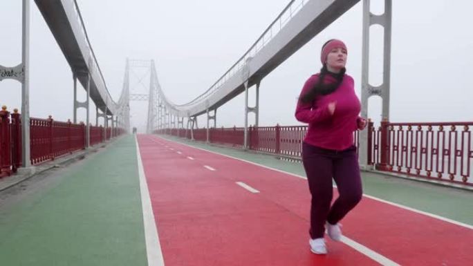 年轻胖乎乎的高加索女孩在桥上奔跑。前镜头慢动作。紫色套装