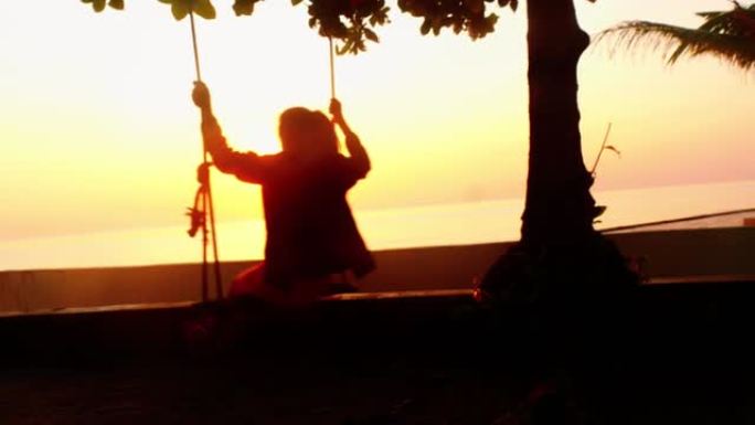 模糊的剪影女孩玩秋千，悬挂在日出背景的树上，慢动作。
