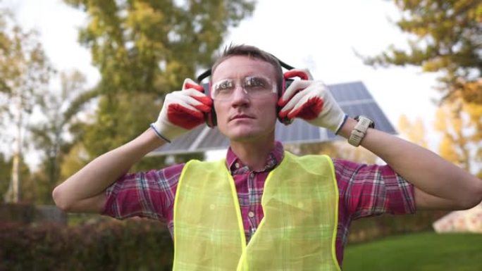 一位戴着耳机的工程师在太阳能站工作。工人在太阳能电池板附近戴上耳机进行声音保护。关心健康，工作安全。