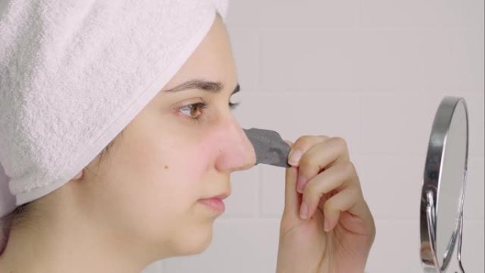 一个女人从鼻子上取下一条清洁条。鼻子上的黑点。浴室里没有化妆的女孩。皮肤护理，问题皮肤，清洁。自然美