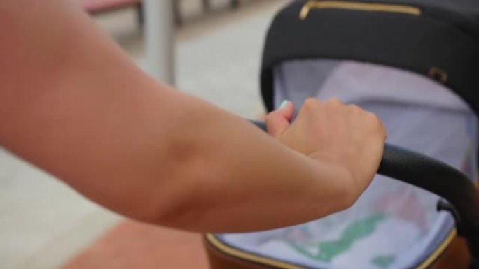 夏天，女性的手在海滨长廊推着婴儿车。家庭、母亲和人的概念。特写镜头。