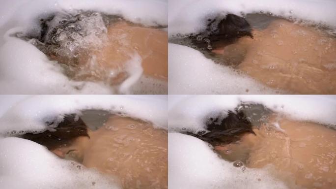 男孩在浴缸里用泡沫沐浴在水中，浸入水中，吹泡泡