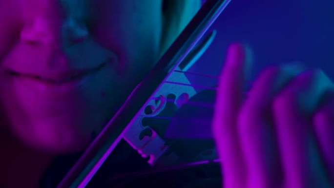 木制小提琴和弓的详细镜头。专业小提琴手在明亮的霓虹灯的背景下演奏古典交响曲。女人的脸和银子工具特写。