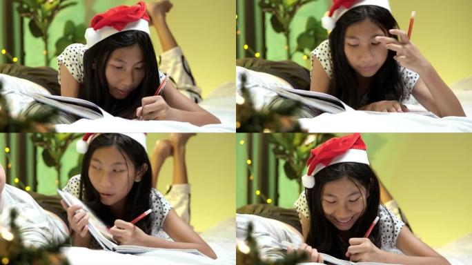 快乐的亚洲女孩戴着圣诞老人的帽子做作业，晚上躺在床上，穿着圣诞装饰品，生活方式理念。