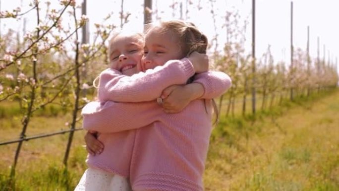 两个穿着相同衣服的双胞胎小姐妹在苹果园拥抱。