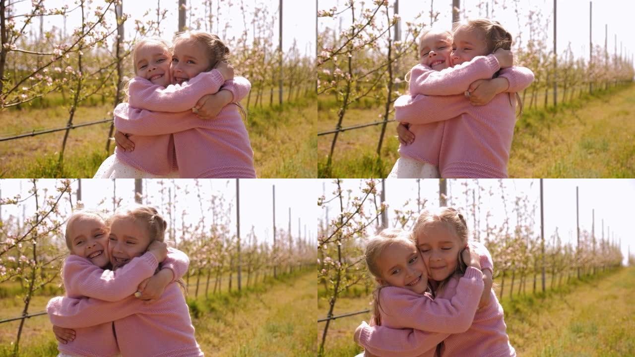 两个穿着相同衣服的双胞胎小姐妹在苹果园拥抱。