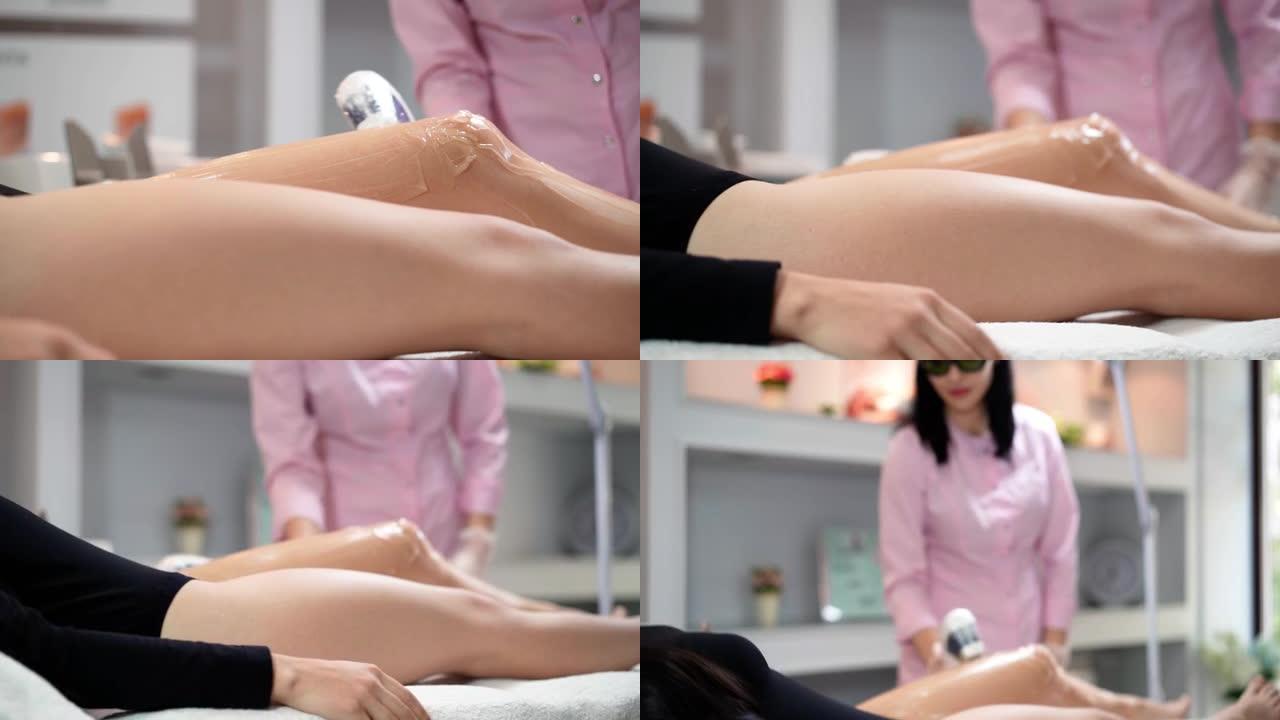 迷人的女性美容师做激光脱毛苗条的腿美丽的年轻女子是躺在一个美容沙龙的医疗沙发上。宇宙学，脱毛和水疗概