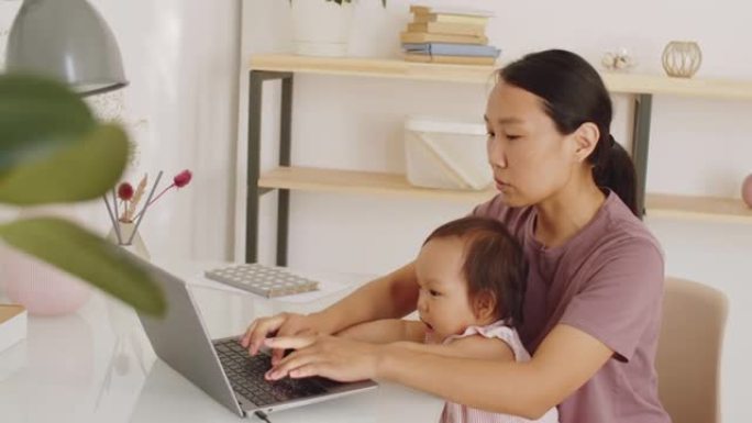 亚洲母亲在家休育儿假在笔记本电脑上工作