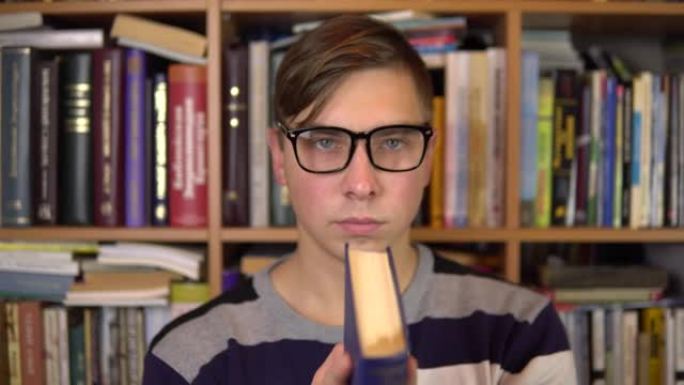 一个年轻人读了一本书，突然在图书馆里猛地。一个戴眼镜的男人仔细地看着书，看着相机。背景是书架上的书。