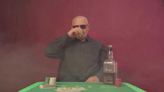 赌场里的一名男子在赌桌旁举起一杯威士忌。