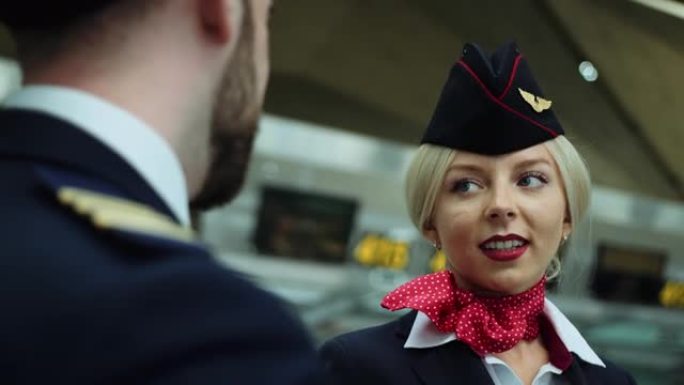 在机场空姐，金发和蔼地微笑着，与飞行员交谈。欧洲妇女穿着深蓝色制服，在她的白衬衫上系着猩红色的围巾。