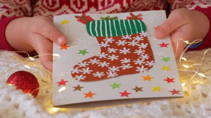 圣诞袜子手工贺卡DIY项目。彩色卡片，带红色圣诞老人袜子糖果礼品袋。孩子在白色针织格子背景上做新年节