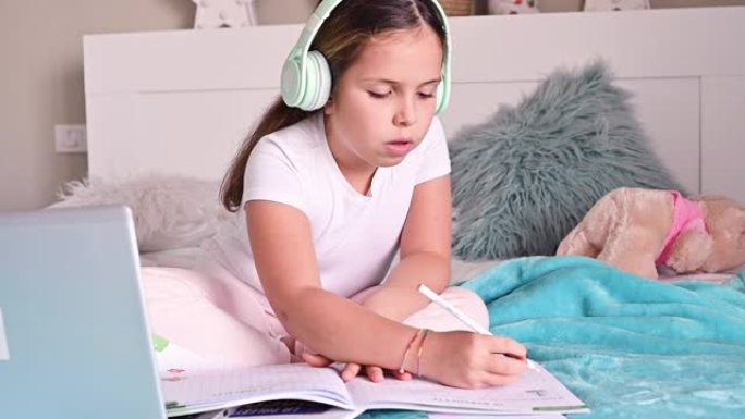 一个小女孩，一个戴着耳机的女学生，带着课本，在电脑上上课。在线课程。检疫时期家庭教育的新版本，cov