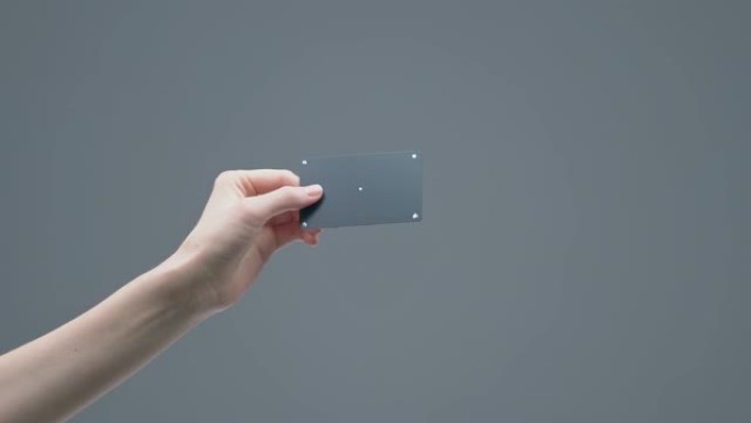 女人的手在灰色演播室背景上显示带有跟踪点的黑色塑料银行卡，广告视频