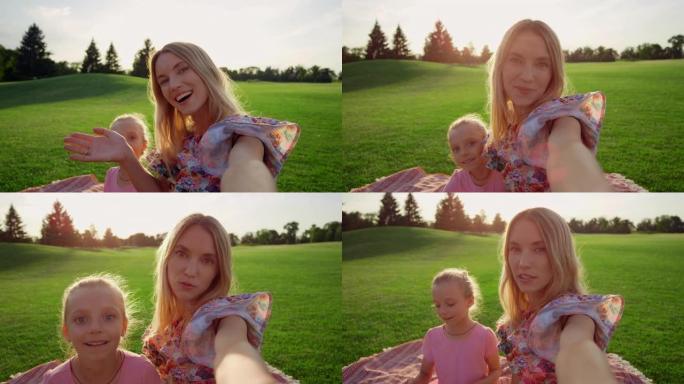 微笑的女人带着女儿在绿草丛中自拍手机。