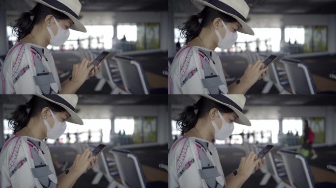 一名戴着防护口罩的亚洲年轻女性游客在国内机场等待航班时正在使用智能手机