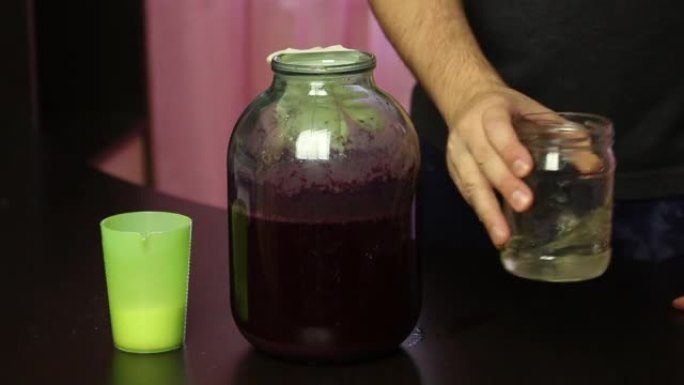 一名男子从一罐葡萄汁中取出橡胶手套。加水加糖。在流行病期间制作自制葡萄酒。