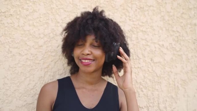 年轻的非洲裔美国妇女在街上戴着耳机。黑人女歌手听着幸福的音乐之声。