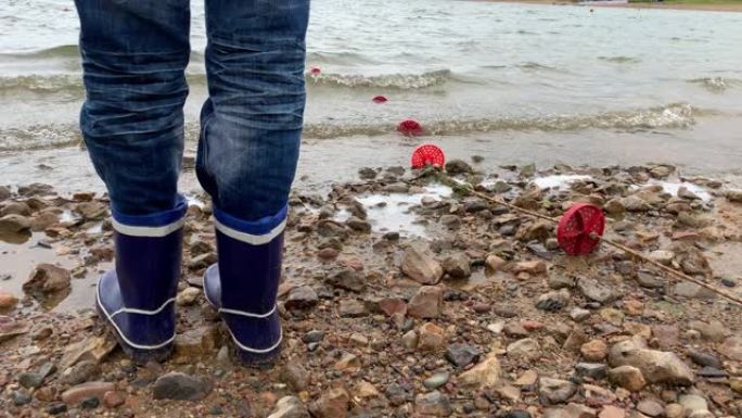一个穿着蓝色橡胶靴的男孩的腿站在湖岸沙滩上，美丽的水景