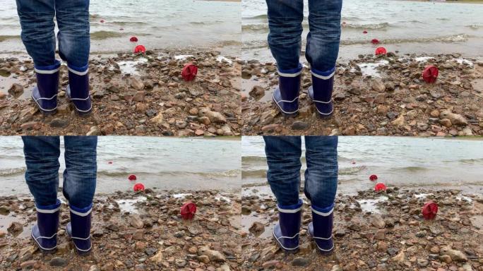 一个穿着蓝色橡胶靴的男孩的腿站在湖岸沙滩上，美丽的水景