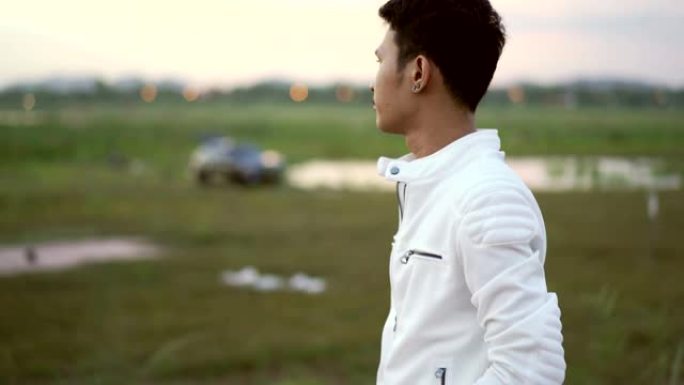 年轻的亚洲男子在日落时站在公园等候某人