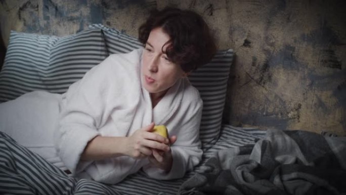 成熟的女人躺在床上，看电视，吃苹果