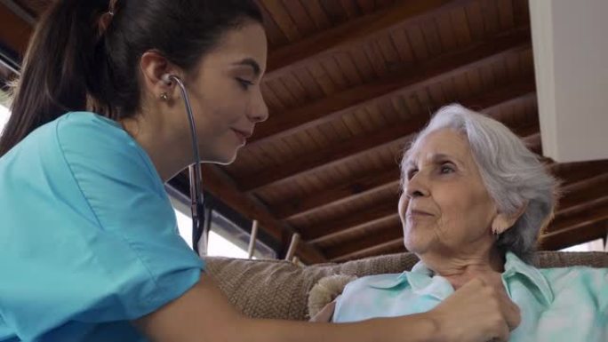 年轻护士在家庭保健访问期间使用听诊器检查老年妇女的心跳