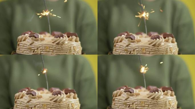 男孩拿着黄色背景上闪闪发光的生日蛋糕，庆祝节日概念。