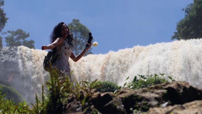 穿着裙子的快乐年轻女子在巨大的瀑布流的地面上跳舞。
