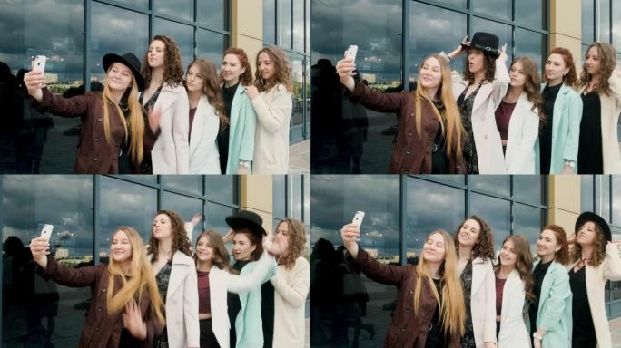 假日和旅游概念-美丽的女孩在城市户外自拍。五个女孩在玻璃窗附近的智能手机上。青春，青春。走在春天。