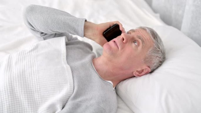 积极的老人在床上用智能手机聊天