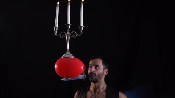 一位马戏团的艺术家在他的嘴里拿着一把刀，一个装有烛台的气球，上面燃烧着蜡烛，并保持平衡