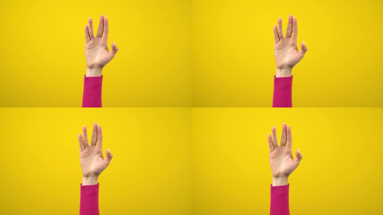 一只女性的手显示出外星人的问候标志。孤立的黄色背景上的工作室摄影。