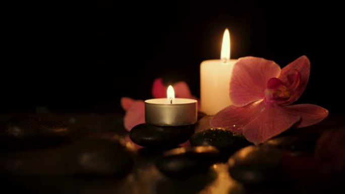 深色背景上有水疗石和兰花的蜡烛。芳香疗法、美容和健康理念