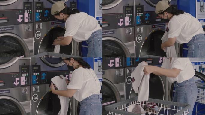 戴着口罩的年轻女子正在自动洗衣店洗衣服。