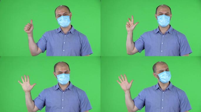 戴着医用口罩的中年男子的肖像显示拳头，然后数一，二，三，四，五个手指。穿着蓝色衬衫的秃头男性在工作室