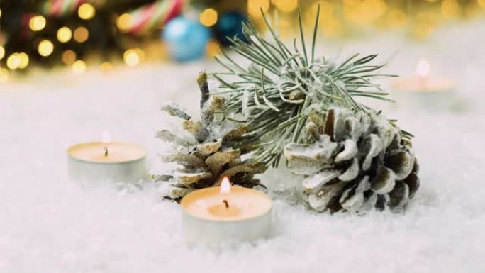 在圣诞节背景下的松果，冷杉树枝和蜡烛上落下雪。