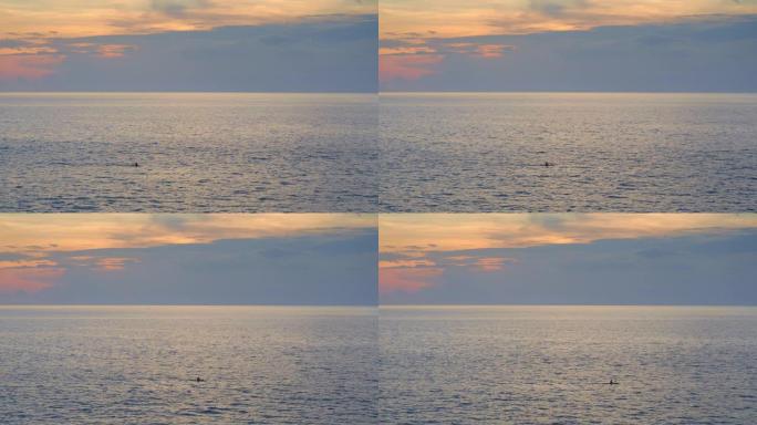 日落时分乌云和黄色天空的小浪在海上皮划艇人的剪影