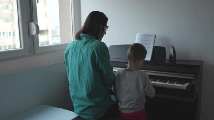 年轻的母亲教儿子在家弹钢琴