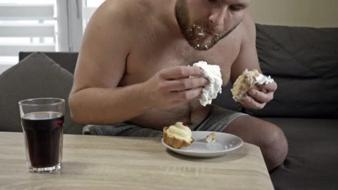 丰满的中年男子贪婪地吃奶油蛋糕。有害的饮食习惯