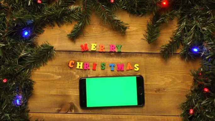 带有绿屏的电话，并在带有闪烁花环的木桌上刻有圣诞快乐的字样。