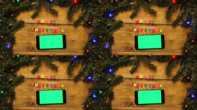 带有绿屏的电话，并在带有闪烁花环的木桌上刻有圣诞快乐的字样。