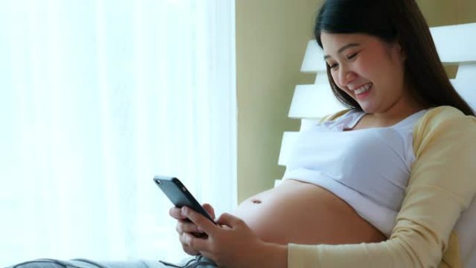快乐的年轻孕妇使用智能手机与丈夫或家人聊天和发短信，说她的婴儿或胎儿身体健康，身体强壮，几个月后会幸