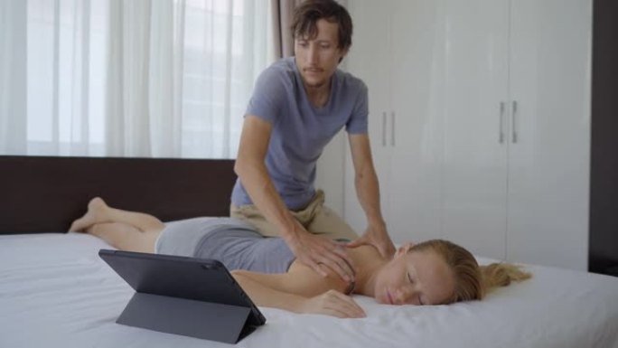 卧室里的一对年轻夫妇。男人通过在平板电脑上观看在线教育视频来学习如何为女人进行身体按摩。在线教育理念