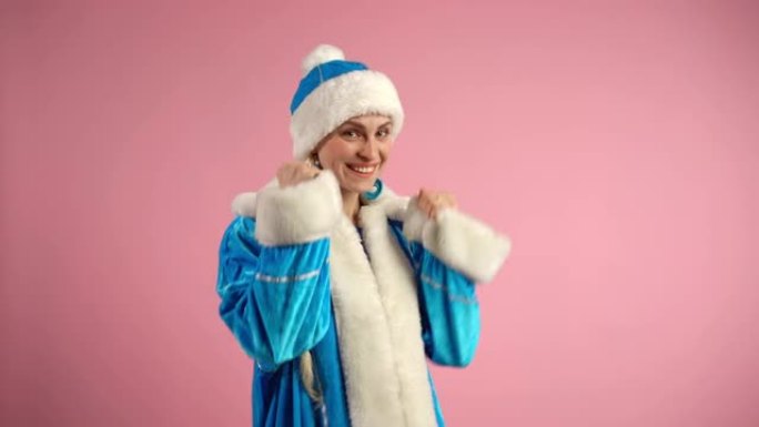 喜出望外的雪少女在孤立的粉红色背景下在相机上显示是手势，微笑着快乐的女人穿着蓝色服装的圣诞老人女人在