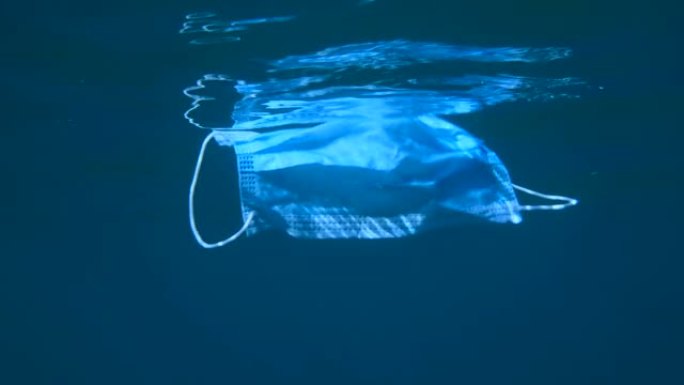 废弃的医用口罩在水面下缓慢漂移。冠状病毒新型冠状病毒肺炎正在造成污染，因为废弃的二手口罩会污染海洋和