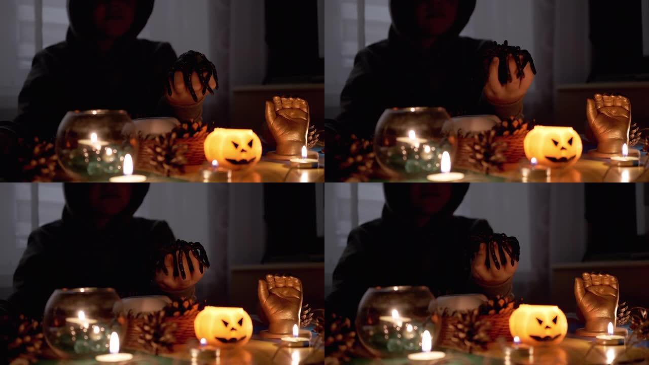 万圣节，戴兜帽的神秘男孩在黑暗的房间里用蜡烛和蜘蛛玩耍