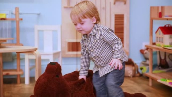 一个开朗的小男孩在房间里玩毛绒玩具，拖着一只大熊穿过地板。